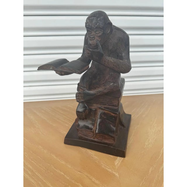 This bronze-toned Darwin’s thinking monkey sculpture depicts a finely detailed ape seated cross‑legged atop a tower of...
