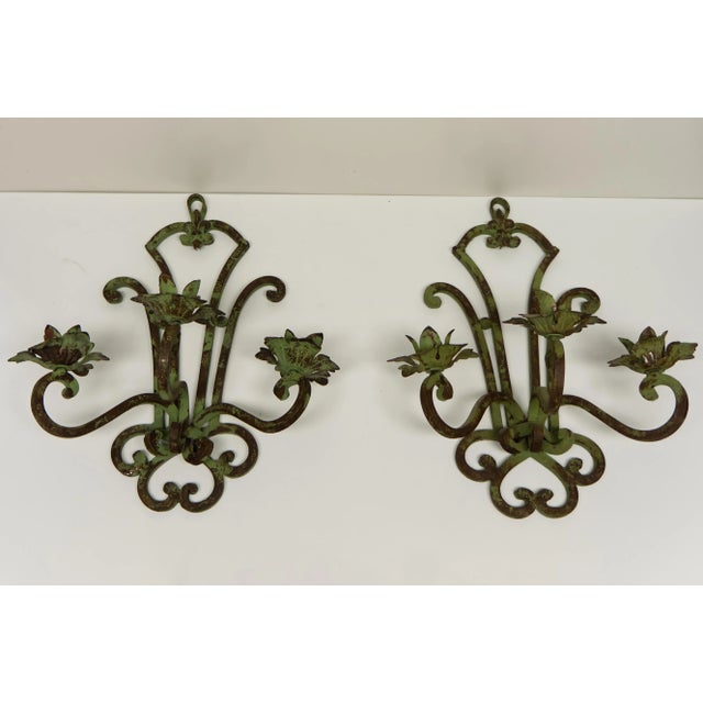 A pair of wrought iron wall sconce candle holders in a verdigris faux finish. Featuring fleur de lis and scrolled details....
