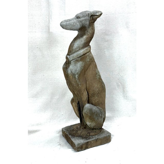 A graceful cast stone sculpture of a seated greyhound, mid 20th century, with a naturally aged surface and serene...