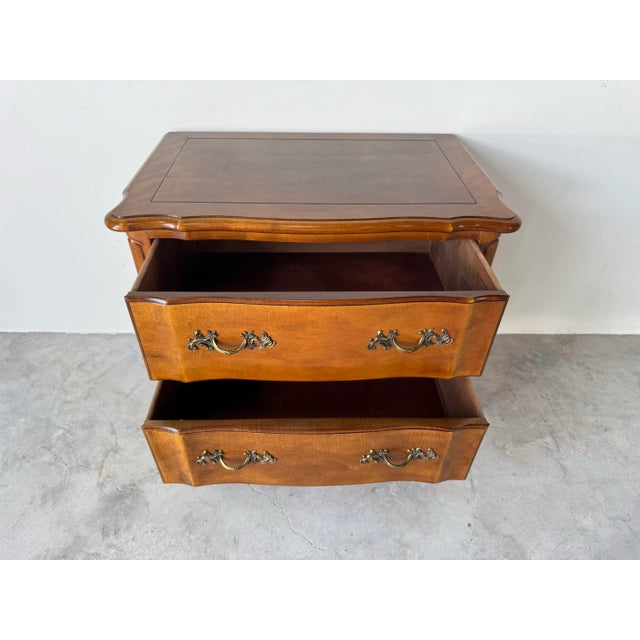 Elegant vintage two-drawer nightstand by Henredon, crafted in the refined Louis XV style. This piece showcases a warm,...