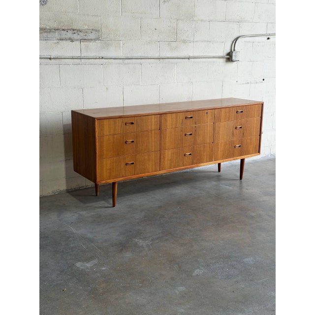 This minimalist lowboy features a wide rectangular frame with a symmetrical configuration of nine stacked storage drawers...