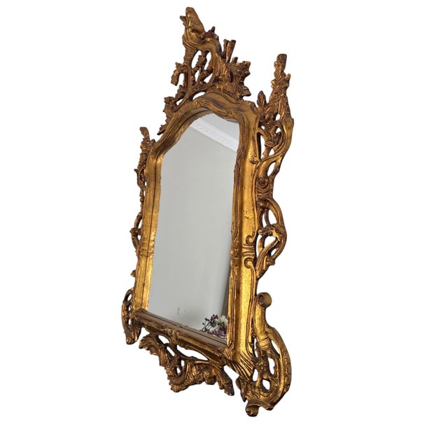 A handsome and richly carved pair of Baroque-style mirrors, finished in a warm, inviting gold tone. Each piece is framed...