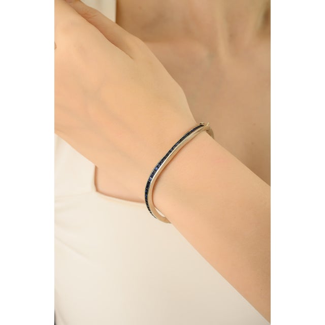 This Channel-Set Blue Sapphire Bangle Bracelet is crafted in 925 sterling silver and adorned with a continuous row of...