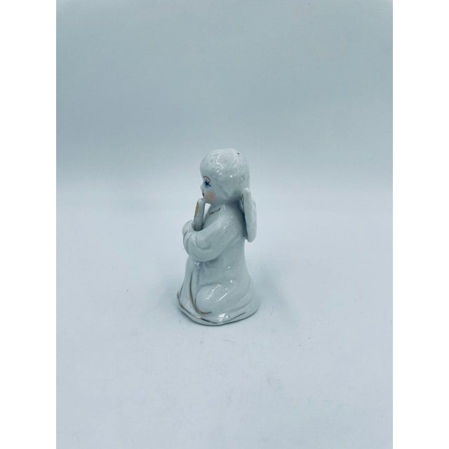 A vintage-style collectible figurine, crafted from high-quality white porcelain. The figurine depicts a small, kneeling...