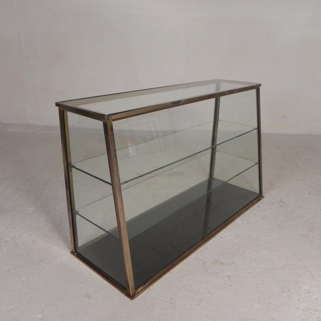 Chic counter display case with 4 glass shelves with different depths. The display case slopes upwards. The sliding doors...