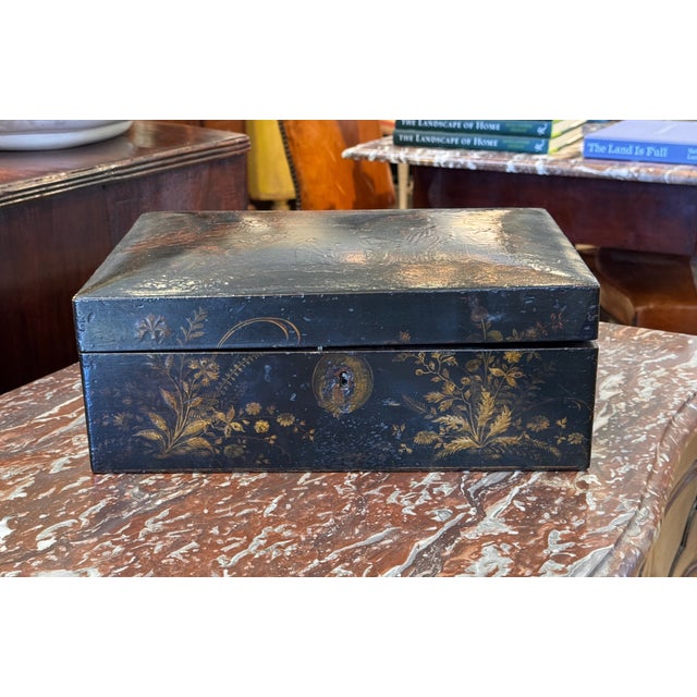 Black lacquered box decorated overall with gilt figures, trees, pavilions, and flowering plants on the sides, and a...