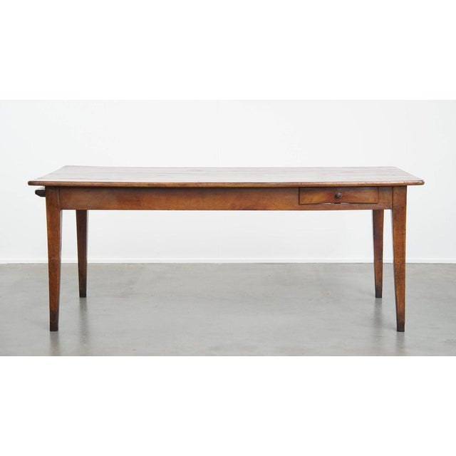 Offered this antique French dining table made of cherry in a warm color with a large extendable top and drawer. This...