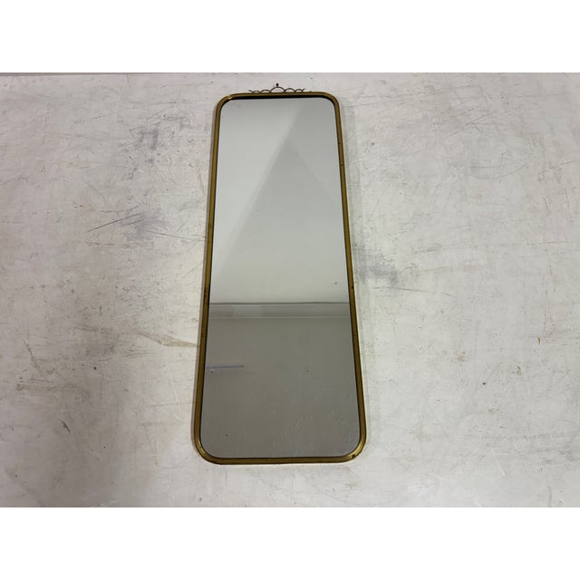 A tall and elegant mid-century brass mirror, distinguished by its restrained form and delicate decorative detail. The...