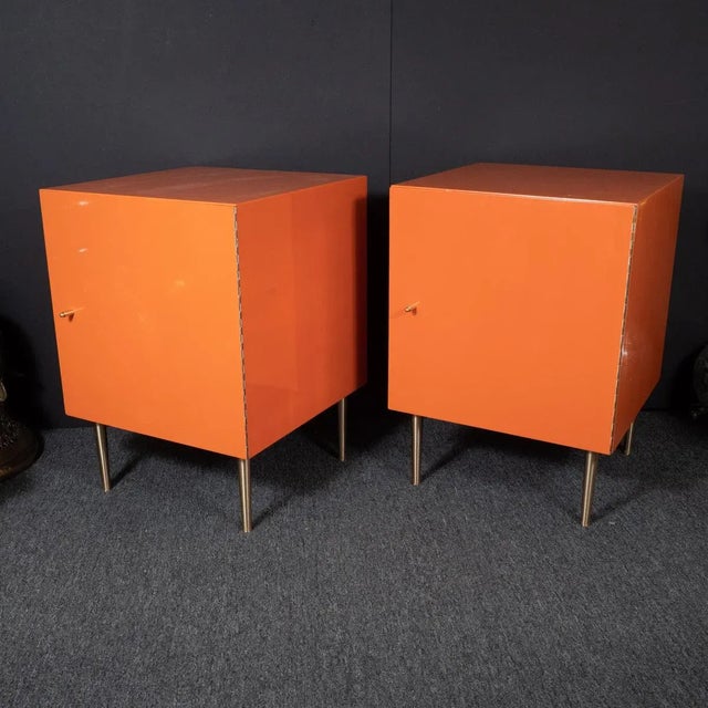 Pair of orange, painted wood cabinets with brass pulls, tapered brass legs and mirrored interiors. Some minor chips in...