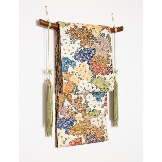 Mid-century Silk Japanese Obi with beautiful chrysanthemum flowers. Displayed on a wooden rod with green tassels....