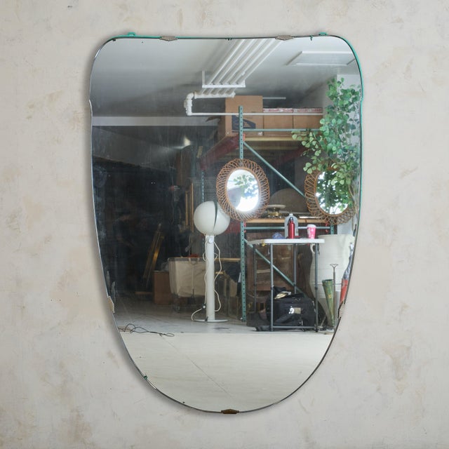 A large-scale 1970s Italian wall mirror featuring a softly rounded form framed in brass, accented by subtle turquoise-...