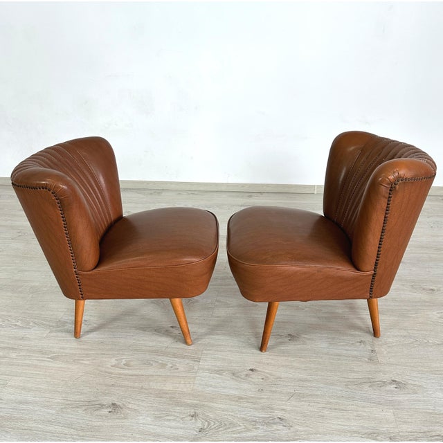 Dimensions: H 25.5” x W 21” x D 22” x SH 16.5” Pair of Vintage Cocktail chairs in brown faux leather with tapered legs....