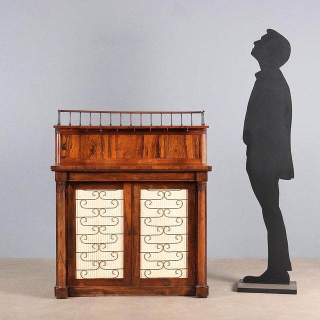 Small bookcase. Front with a pair of doors with pleated fabric panels and brass scrollwork, flanked by turned columns. The...