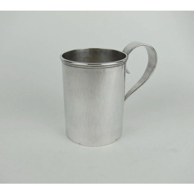 A pair of heavy sterling silver mugs with spot hammered surfaces and strap handles from the Arts and Crafts period by...