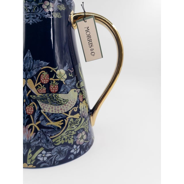 A striking Morris & Co. “Strawberry Thief” porcelain pitcher, finished in a rich navy ground with elegant gold-toned...