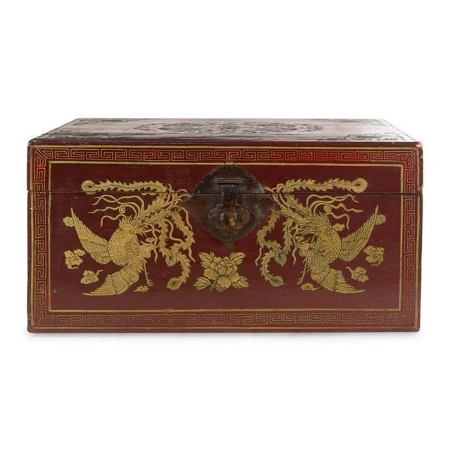 This small blanket box is in wood, covered in red lacquered leather, and beautifully decorated in gold on the front...