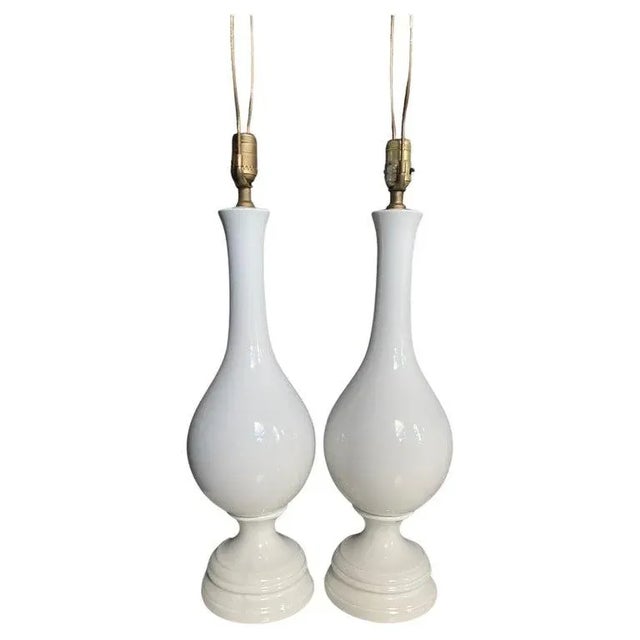 Pair of Mid Century Modern white ceramic glazed table lamps. These classic vase shaped pottery lamps feature a gloss white...
