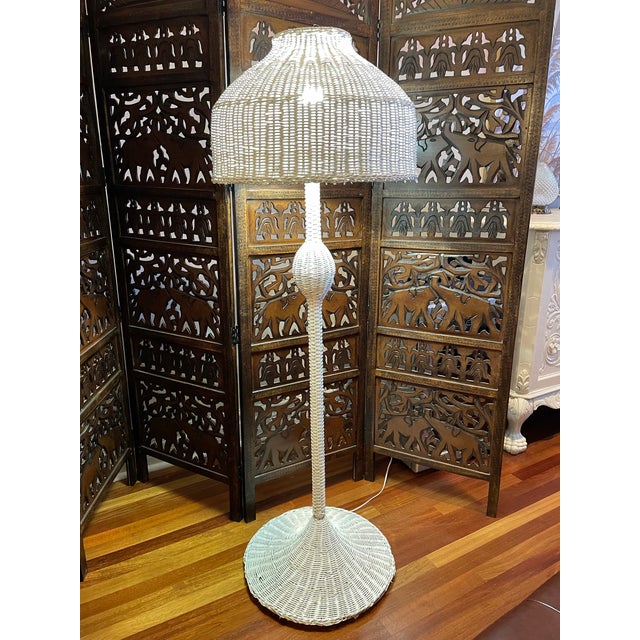 Vintage 1970s wicker floor lamp with a sculptural shade and pedestal base, finished in a soft white tone. The silhouette...