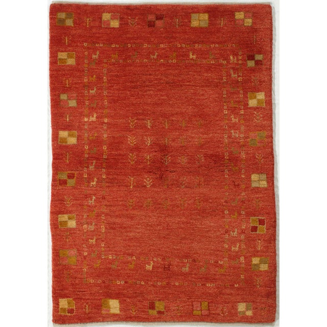 Vintage Persian hand-knotted Gabbeh wool rug featuring a rich red field with small tribal motifs and stylized animals...