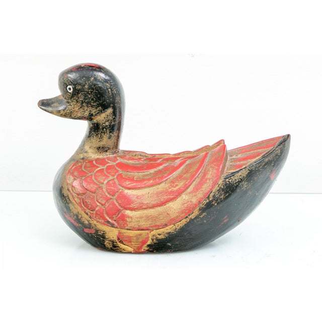 A pair of vintage hand-carved wooden ducks painted in black, red and gold with a worn, distressed finish, rounded body,...