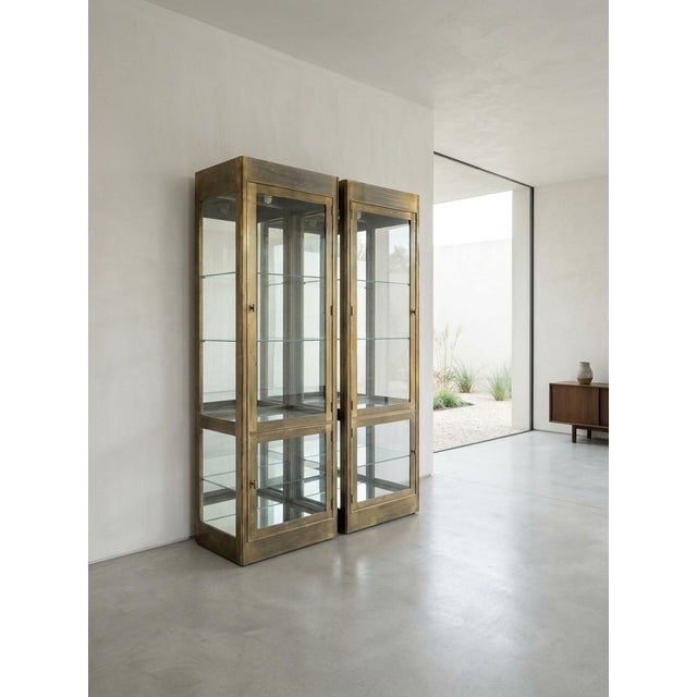 This image displays a pair of Mid-Century modern brass and glass illuminated vitrines, highly characteristic of luxury...
