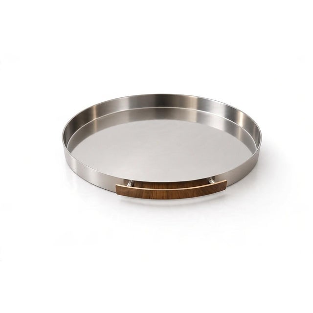 Round serving tray in stainless steel with a low, straight edge and two curved handles. The understated shape and finely...