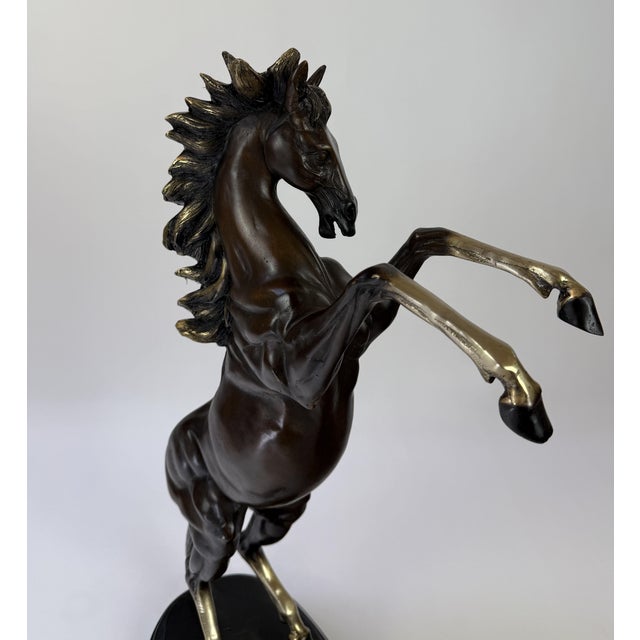 A striking bronze sculpture of a rearing horse, captured mid-motion in a powerful, elevated stance. This prancing stallion...