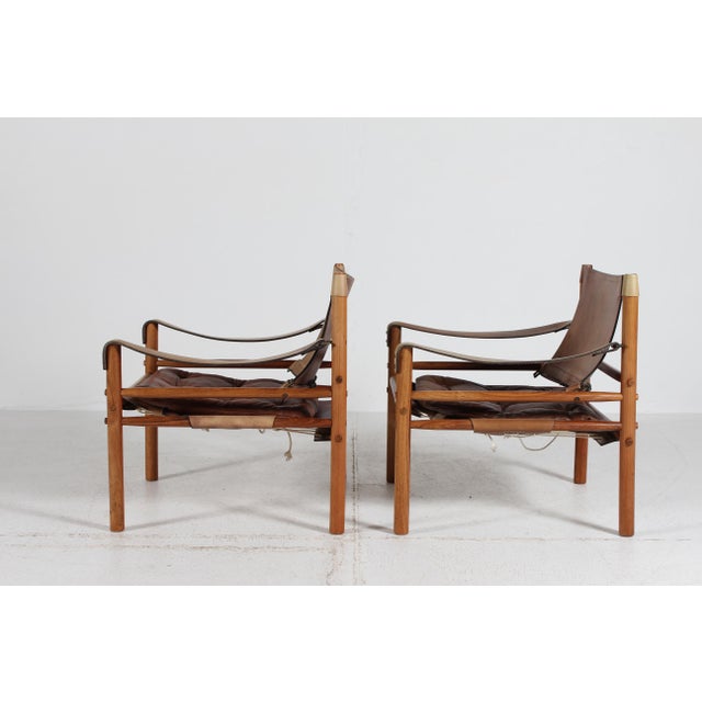 A Pair of Scirocco Safari easy chairs by Arne Norell (1917-1971). They are made of solid rosewood mounted with patinated...