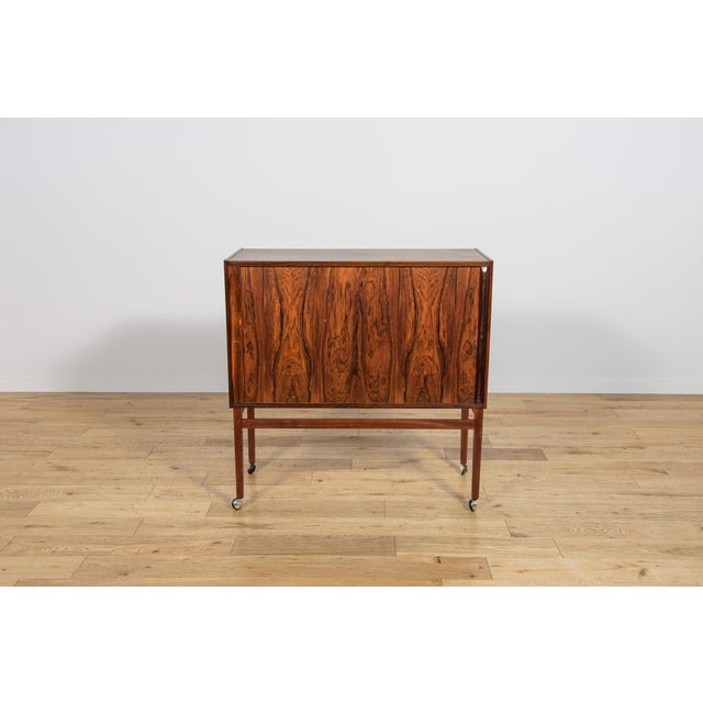 This rosewood bar features roller shutter doors with a key lock. Manufactured in Denmark in the 1960s, this piece of...