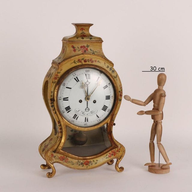 Lacquered and gilded wooden pendulum clock with polychrome decorations of flowering branches. Enamelled metal dial with...