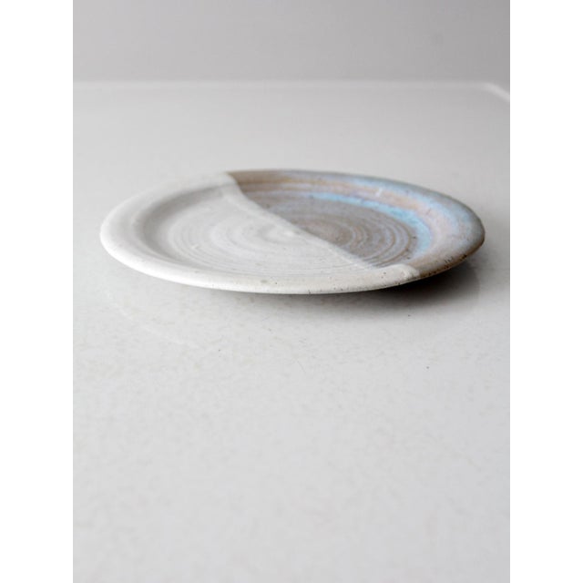 This vintage studio pottery plate features a striking half-glazed design, with one side in a creamy off-white and the...