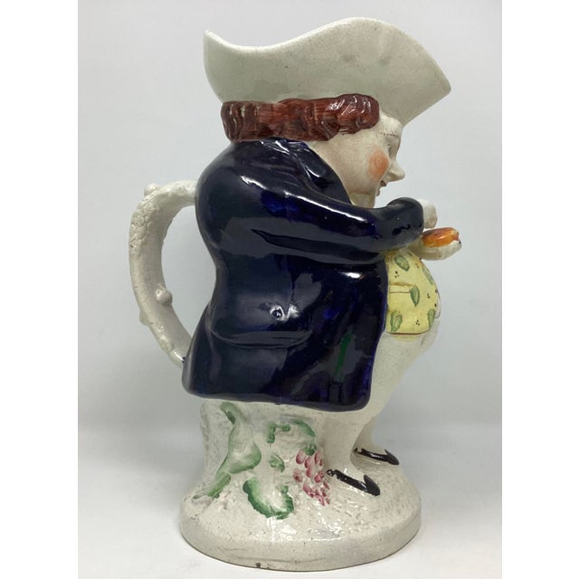 1870 Drinking jug is modelled as a man with a white tricon hat, standing with red hair, holding a snuff box. Well...