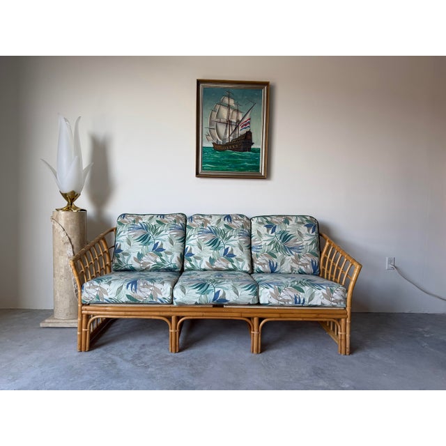 This vintage bamboo and rattan sofa, designed in the style of Ficks Reed, features a classic coastal and tropical...