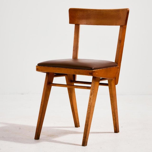 Oak chair with angular shapes and faux leather upholstery from the 1970s. The surface of the chair has scratches and wear.