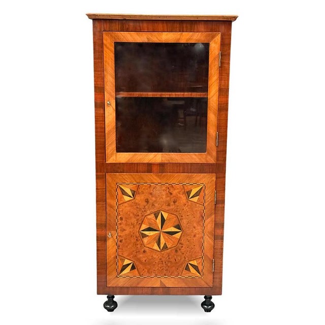 An elegant corner display cabinet or small bookcase from Baroque period, dating to around 1820. The piece is veneered in...