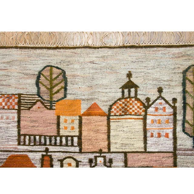 A beautiful mid-20th century Polish Folk Art Cepelia rug depicting a village with rows of houses and churches, and sylized...