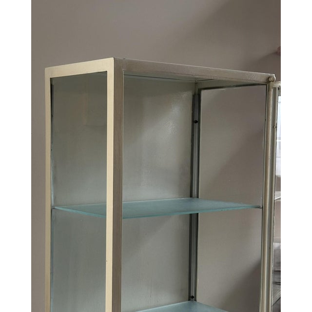 Display cabinet dating back to the 1950s/1960s, made in Italy. It features an ivory-painted iron frame and three glass...