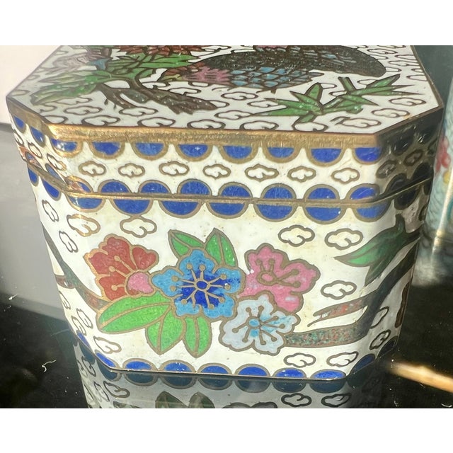 A charming miniature Chinese enamel box featuring a pair of birds nestled among colorful blossoms, leafy branches, and...