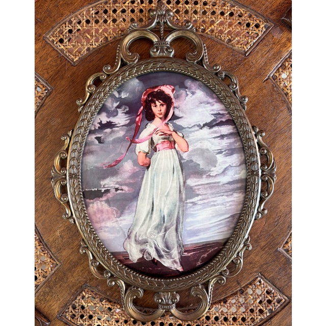 This is a vintage reproduction of Thomas Gainsborough’s “Pinkie,” displayed beneath convex glass in an ornate brass-tone...
