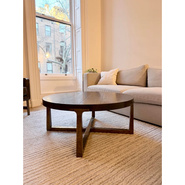 Dark brown oak and brass round Restoration Hardware coffee table. Richly grained American white oak rests on tapered...
