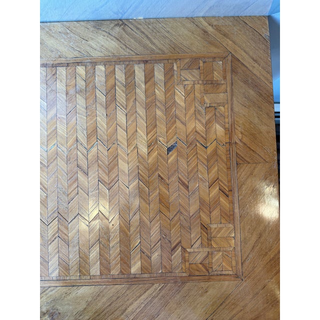 This is an antique marquetry table. It has brass handles. There are striping details on the drawer, and on the top. It has...