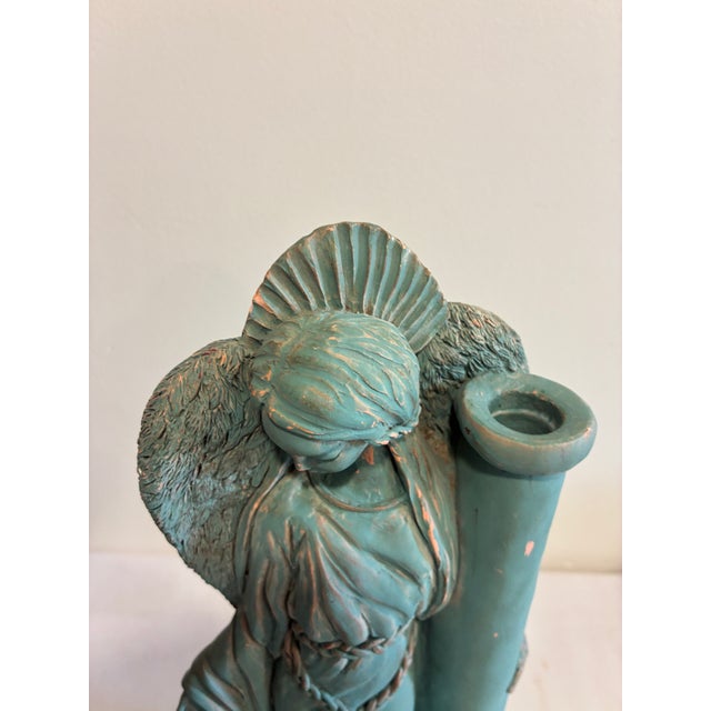 A sculptural terracotta angel candle holder finished in a rich verdigris patina, with terracotta showing through at the...