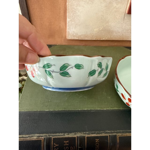 Set of two vintage porcelain bowls featuring a soft celadon glaze with hand-painted floral detailing in iron red and leafy...