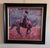 This artwork captures a dynamic moment of a cowboy on horseback, skillfully handling a pink rope amidst a vibrant,...