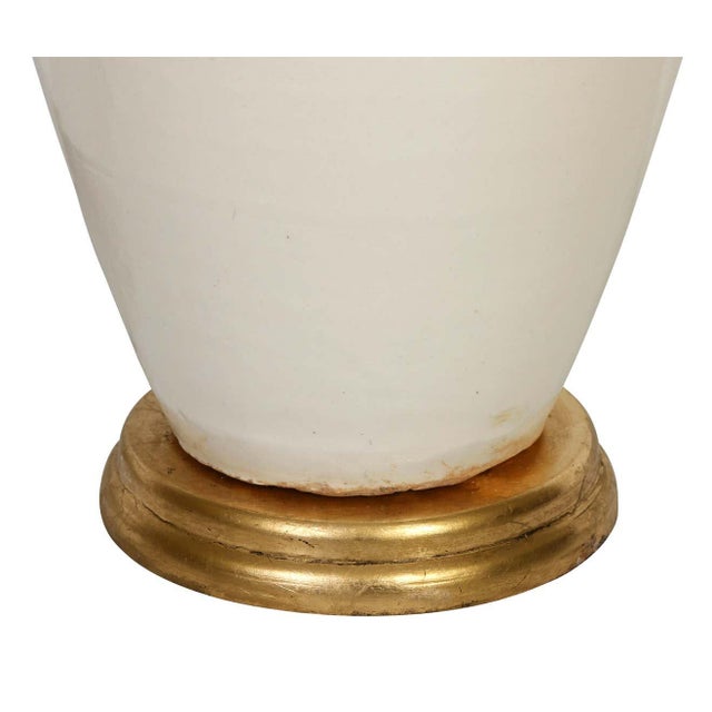 A ceramic lamp in a lovely cream-colored glaze with a graceful silhouette. The warm giltwood base gives the lamp a soft...
