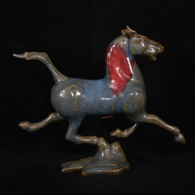 A striking Chinese ceramic sculpture featuring a dynamic horse in a galloping pose, with one hoof resting lightly on a...