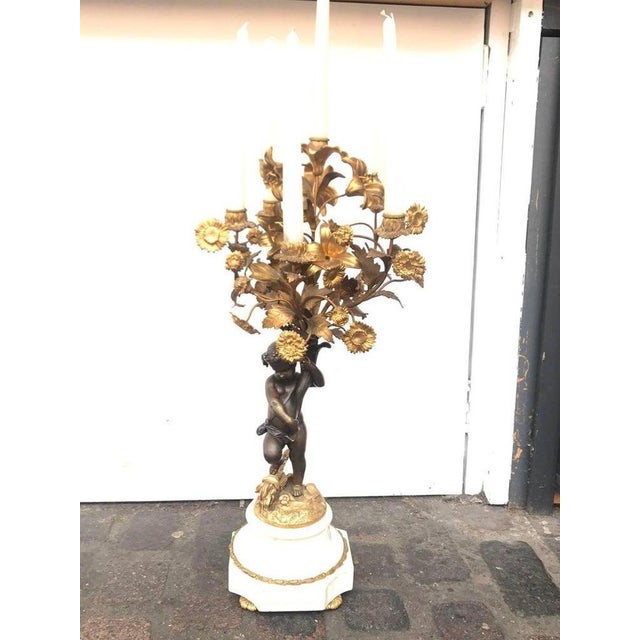 A pair of French 19th century cast bronze putti (cherub) candelabras. The four branch candelabras feature a standing...
