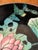 Hand painted porcelain bowl with Lotus flowers in pink and green on a black background. The brass wrap has a hanger. This...