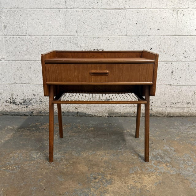 A vintage Danish teak nightstand with a compact raised form, single drawer, and lower string shelf. The piece has a simple...