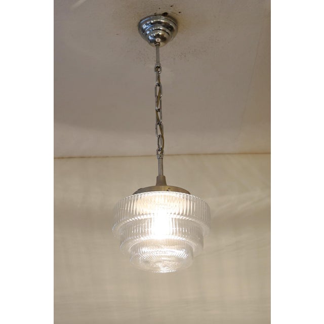 Art Deco lamp, circa 1920. Nickel-plated brass body, suspended by a chain. Step-shaped, grooved clear glass shade. The...